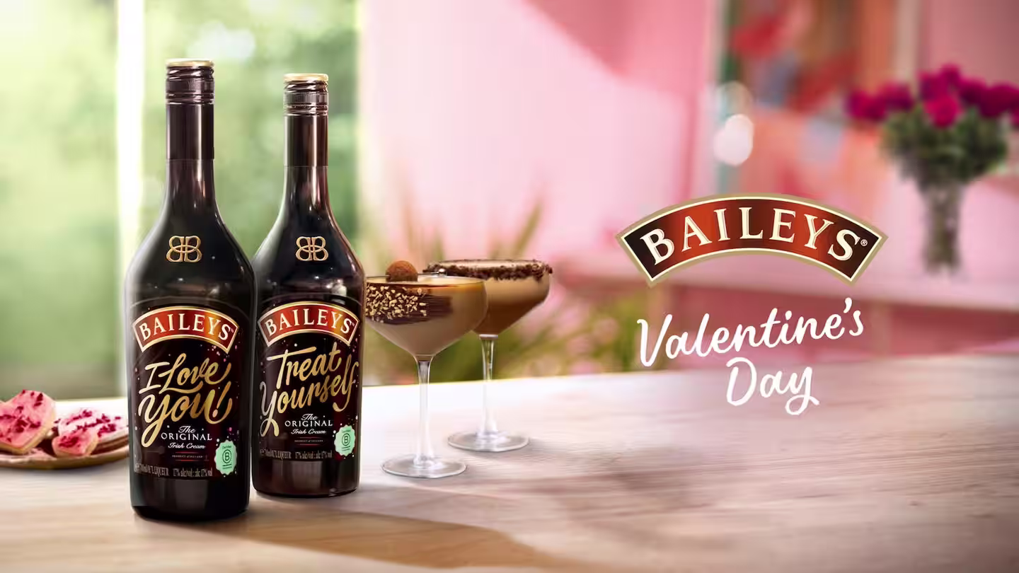 Two Baileys Original Irish Cream bottles with chocolate cocktails, cookies, and flowers on a romantic Valentine's Day-themed background.